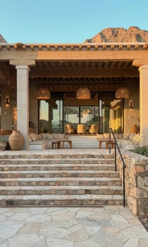 Âme Bohème Residence desert exterior featuring stone and flagstone steps, covered patio with timber beam roof, woven pendant lights, and integrated stone masonry walls set against Camelback Mountain